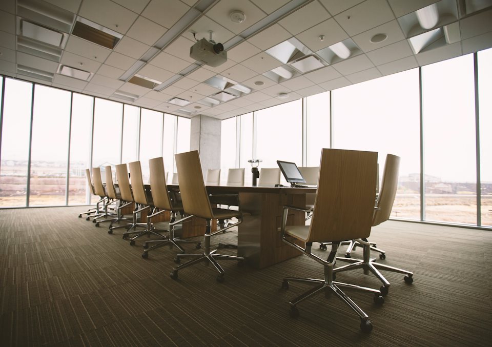 An empty boardroom with a long table and floor-to-ceiling windows
